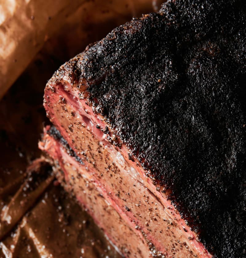 Smoked brisket with a black peppery bark and a pink smoke ring, on butcher paper.