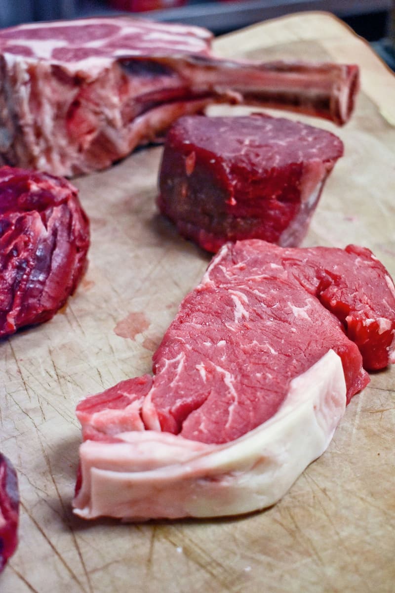 Raw sirloin, fillet and a bone-in rib steak on a working butcher block.