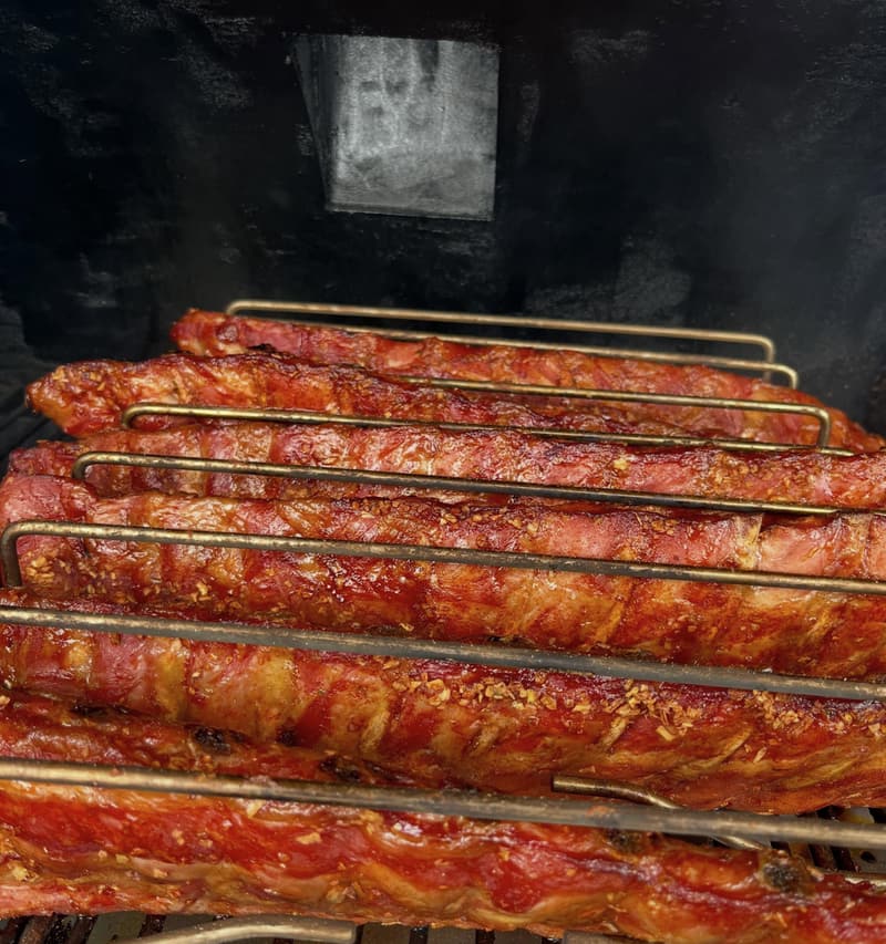 Baby back ribs on a rack in the smoker, the bark caramelised and glossy.