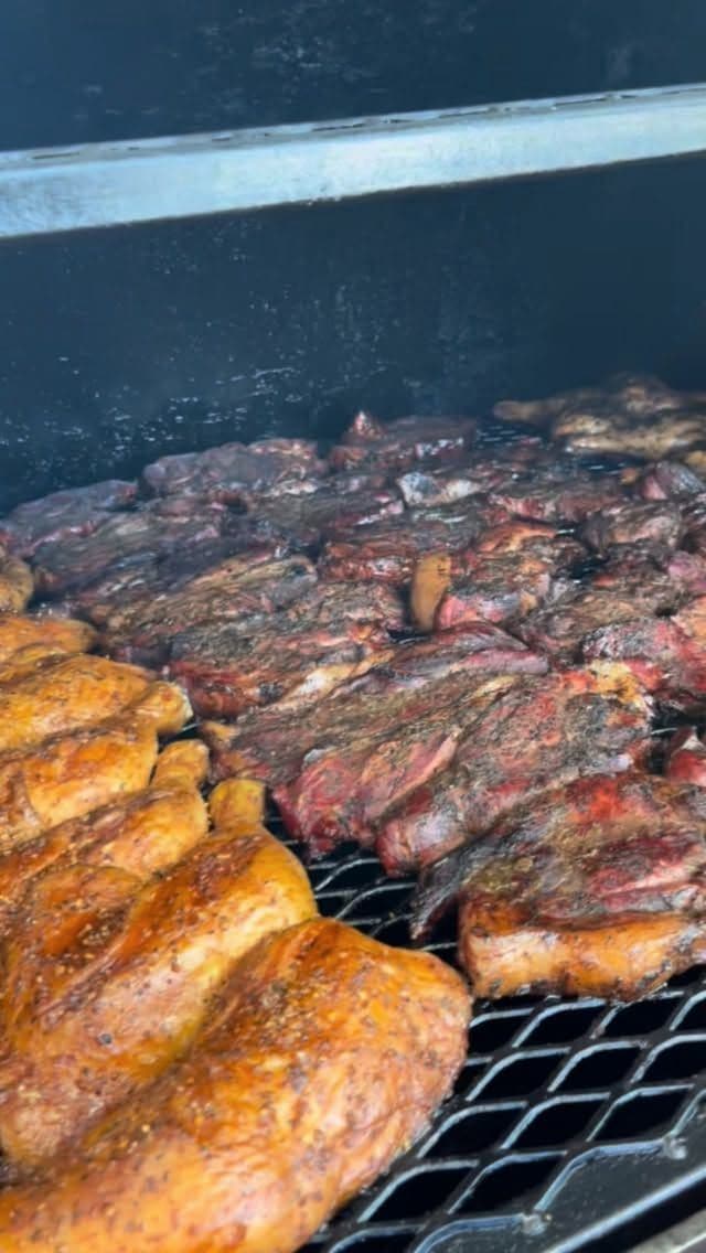 Chicken and pork cooking side by side on the smoker grate.