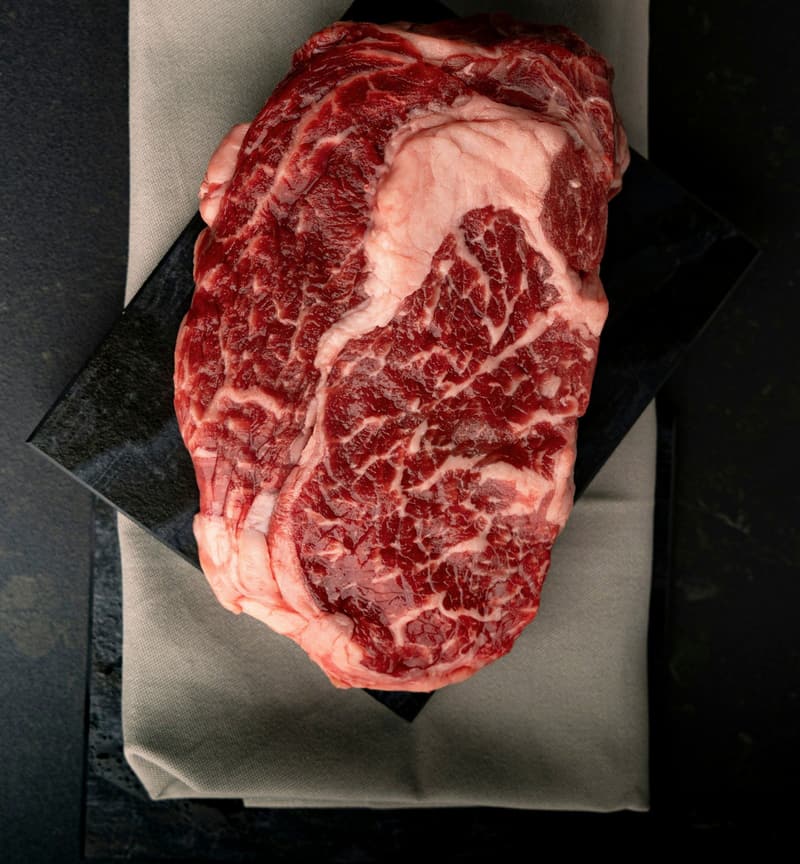 A thick raw ribeye with heavy marbling on black slate.