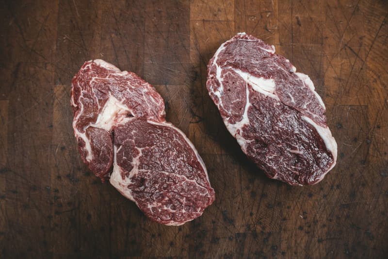 Two raw ribeye steaks with rich marbling on a scarred wooden butcher block.