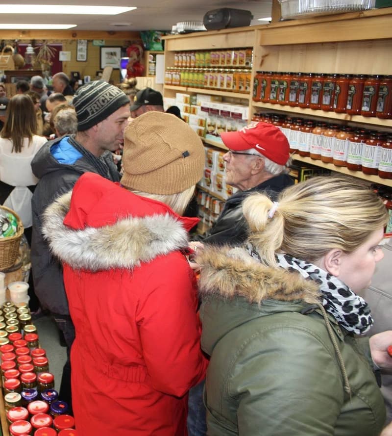 The store packed with shoppers in winter coats at Christmas, in front of shelves of sauces and preserves.